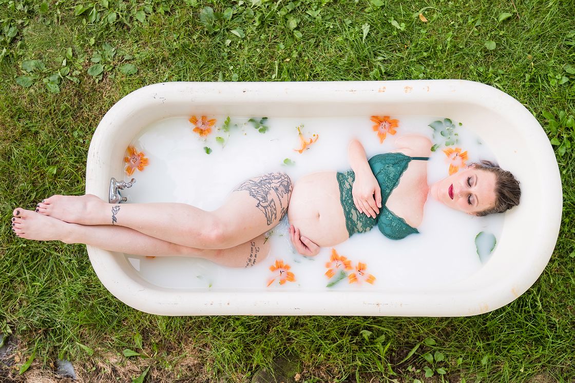 Pregnant woman wearing a two piece blue lingerie posing for a photo while submerged on a milky water in a bathtub