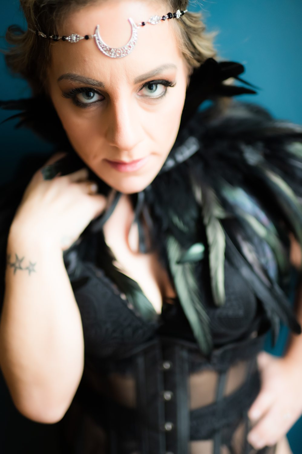 Woman wearing black leather lingerie with a feather top with moon crescent headpiece