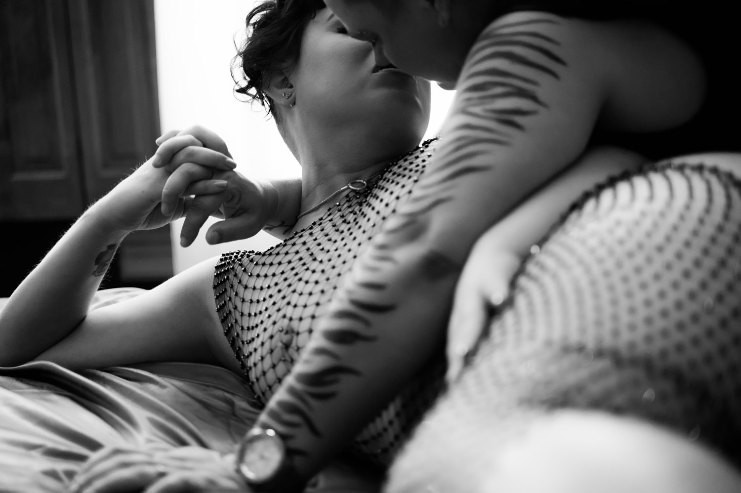 Black and white photo of a couple kissing while posing lying down on a bed