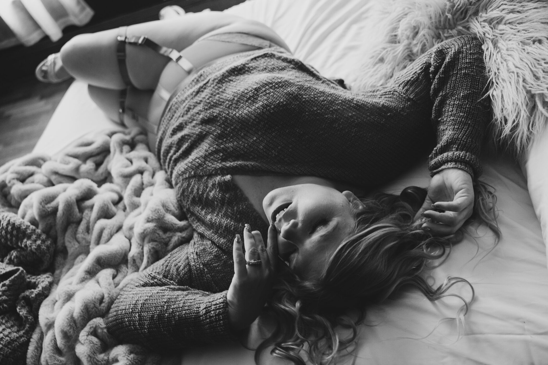 Black-and-white photo of woman lying in-the-sheets wearing a knit sweater and lingerie.