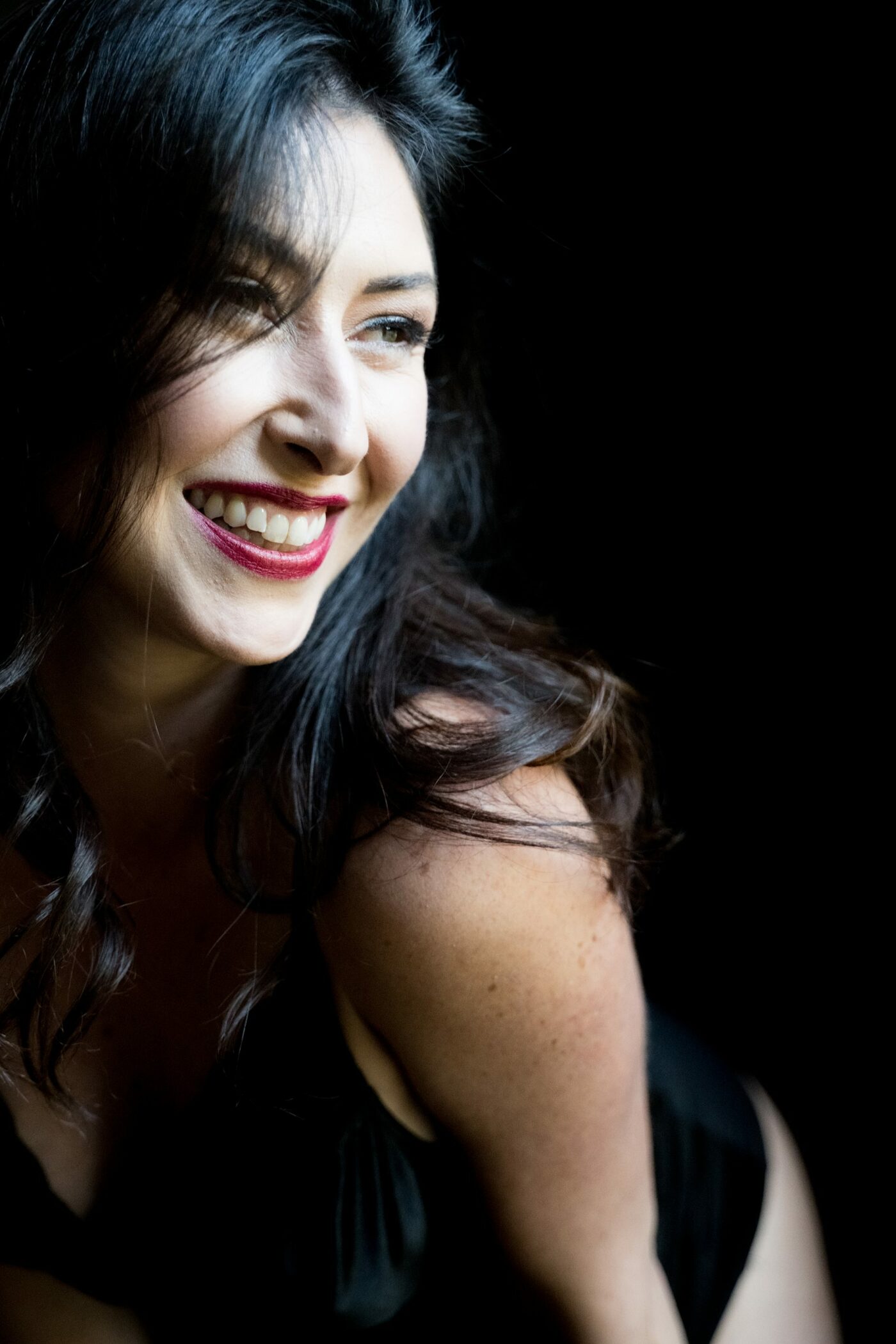 Joyful close-up of woman in black lingerie looking away from the camera smiling during soulful boudoir session in Kalamazoo.