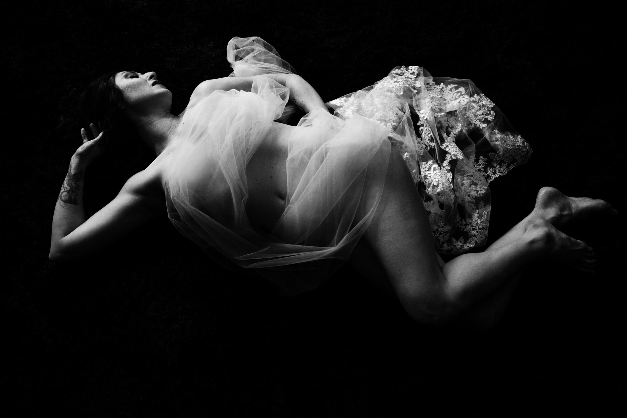 Fine art black-and-white photo of woman lying with her hand on her hip during self-discovery boudoir session.