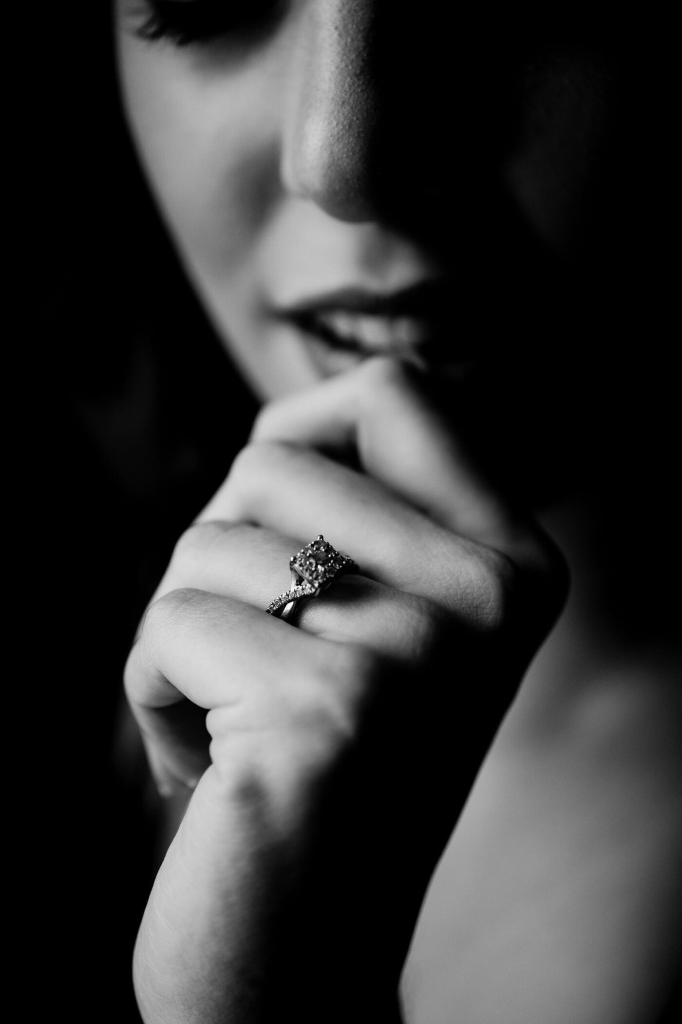 Seductive close-up of woman wearing wedding ring, biting her thumb during intimate boudoir session.