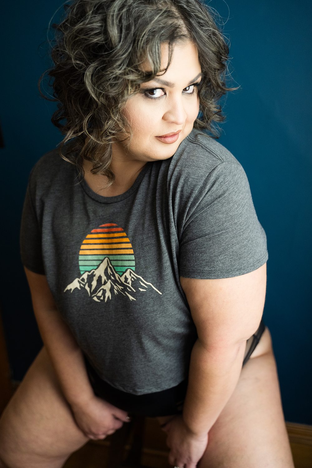 Boudoir photo of woman in her 40s playfully smirking sitting on a stool during Michigan confidence-building boudoir session.