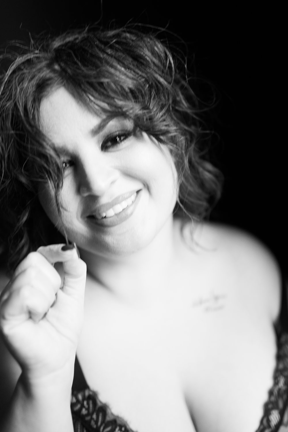 Close-up boudoir portrait of woman smiling at the camera playing with a strand of curled hair.