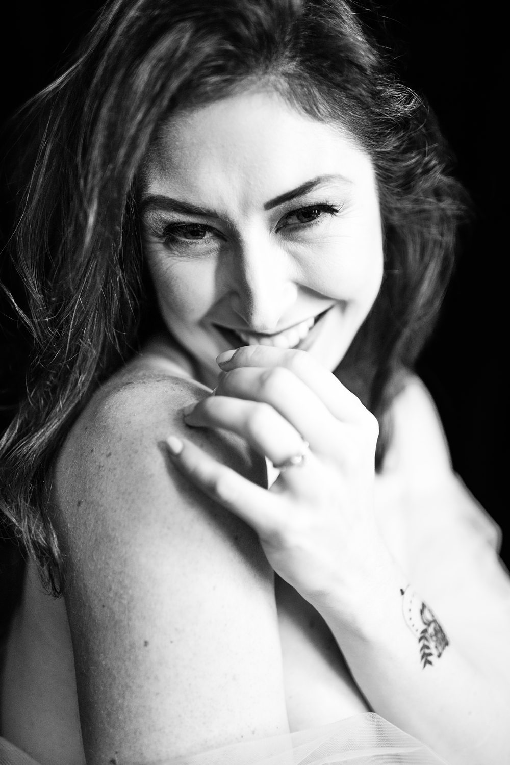 Close-up portrait of woman shyly smiling at the camera, photographed in black-and-white.