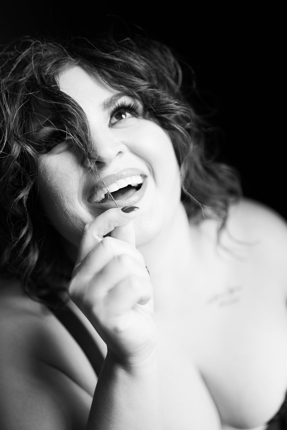Joyful close-up portrait of woman playing with her hair smiling during self-discovery boudoir session in Kalamazoo.