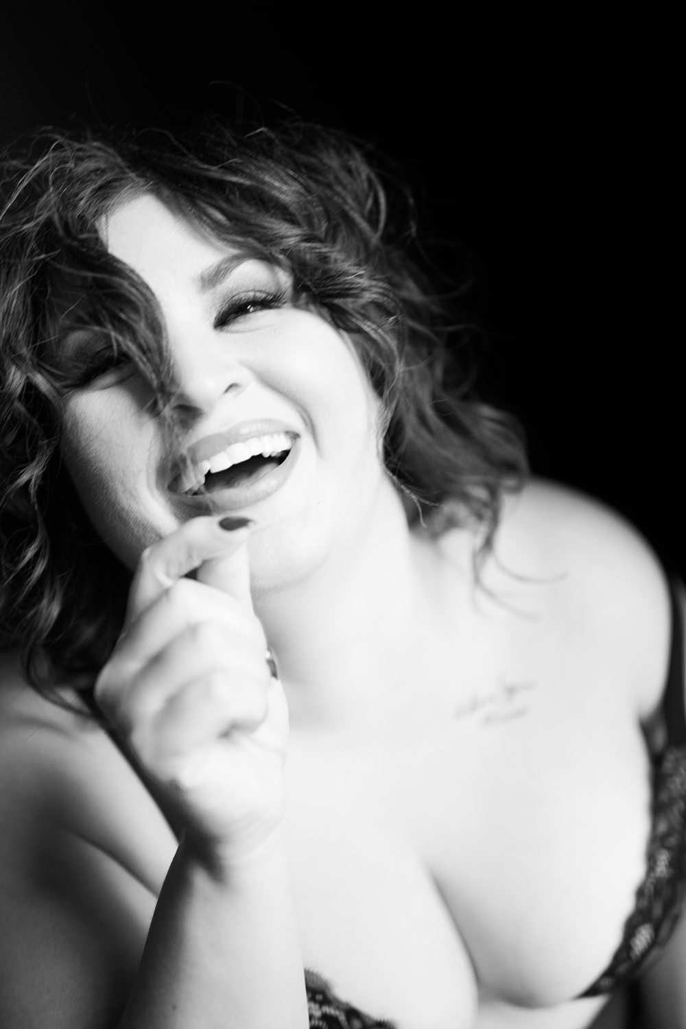 Playful black-and-white boudoir photo of woman in her 40s laughing at the camera.