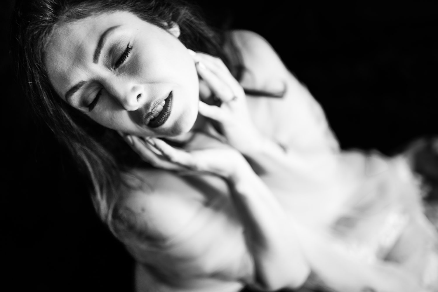 Soulful black-and-white bridal portrait of woman in her 40s gently caressing her face, wrapped in a tulle veil.