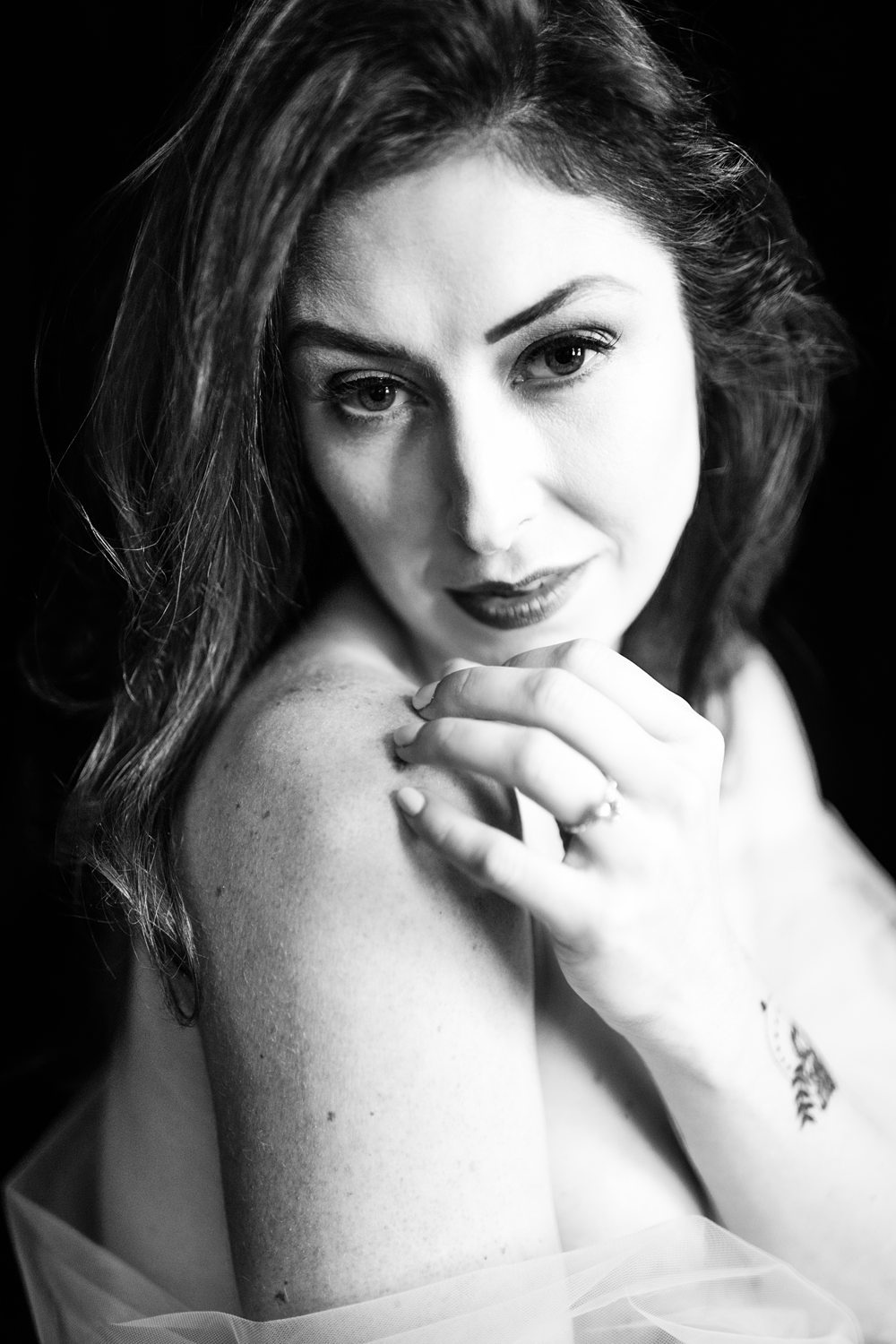 Timeless boudoir photo of woman draped in tulle, gently touching her shoulder photographed in black-and-white.