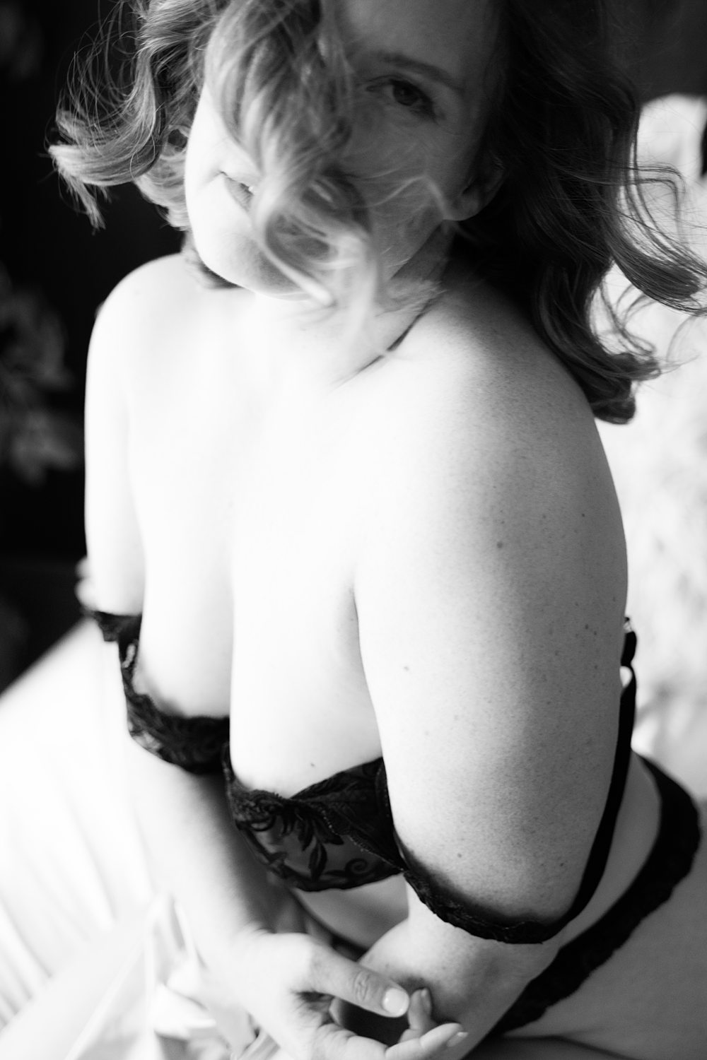 Classic black-and-white close-up portrait of woman in black lace bra with hair waving in her face during empowerment boudoir session.