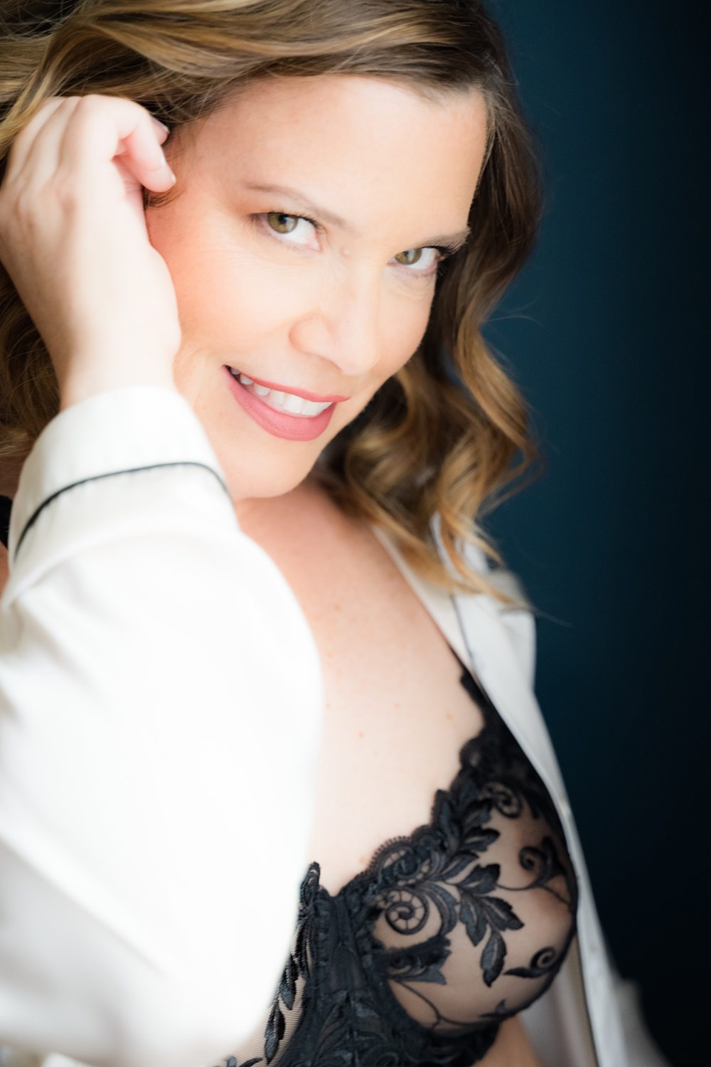 Close-up boudoir photo of woman in her 40s wearing a black lace bra smiling at the camera.