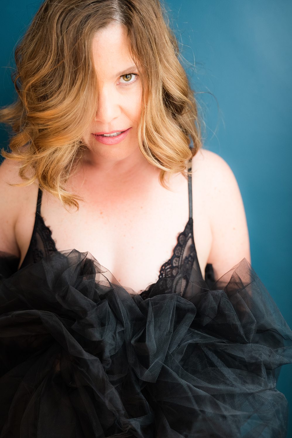 Dramatic portrait of woman smirking confidently at the camera holding black tulle skirt to her chest during empowering boudoir session in Kalamazoo.