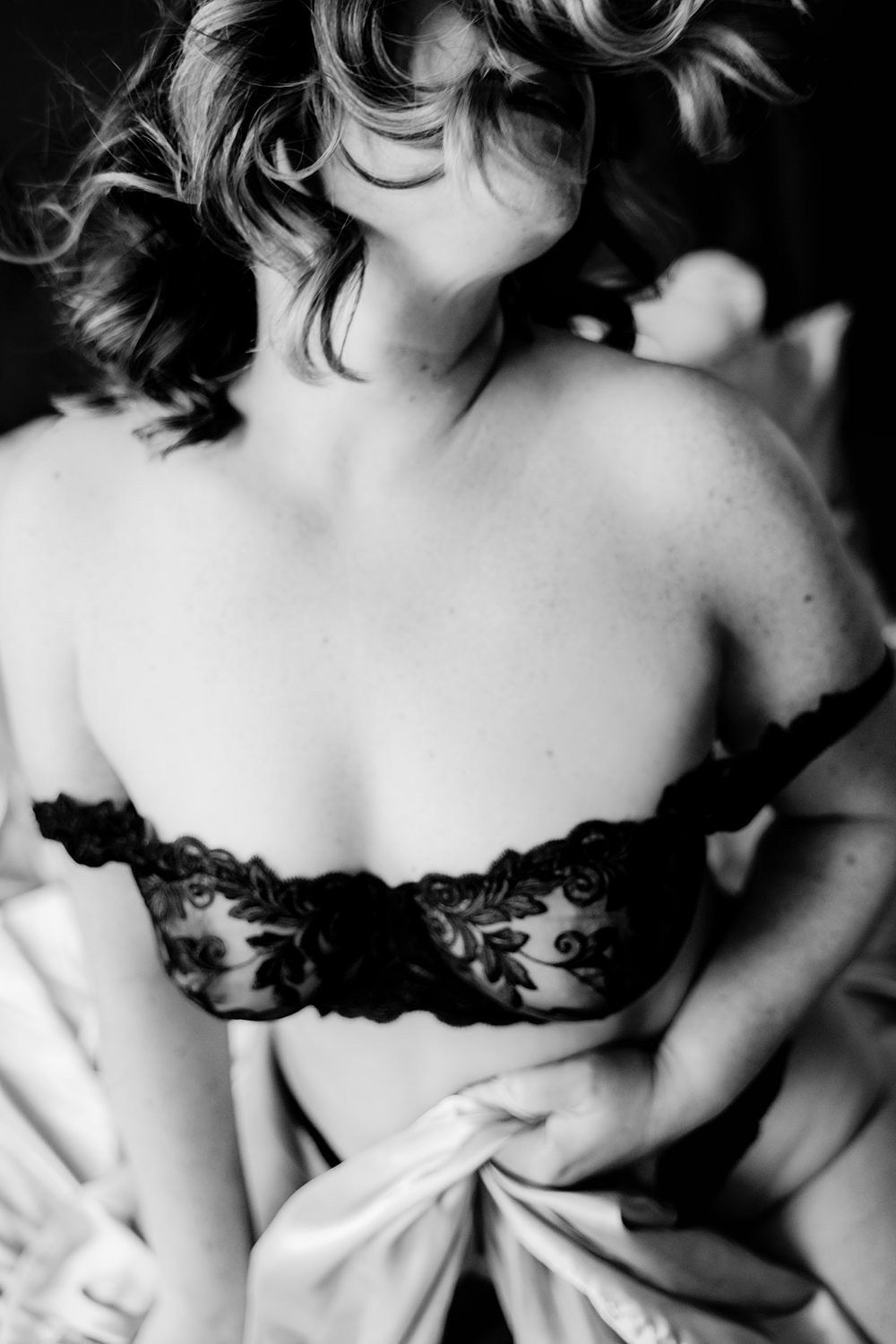 Emotive black-and-white boudoir photo of woman kneeling in-the-sheets wearing black lace bra.