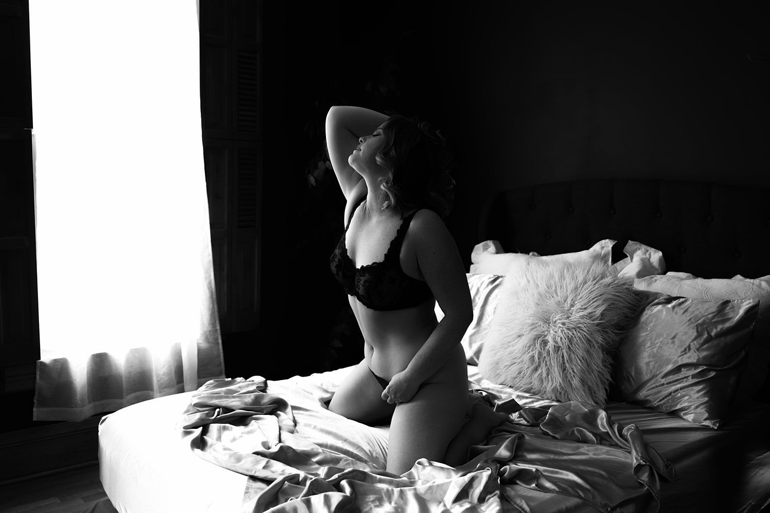 Empowered woman in her 40s kneeling confidently on bed during self-discovery boudoir session in Kalamazoo.