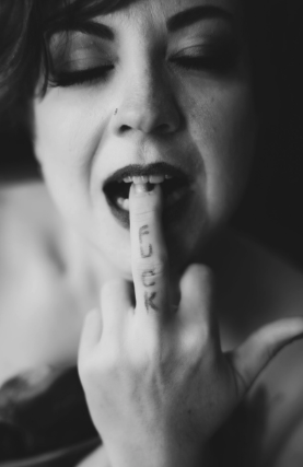 Edgy black-and-white portrait of woman biting her middle finger with the word FUCK written in lipstick.