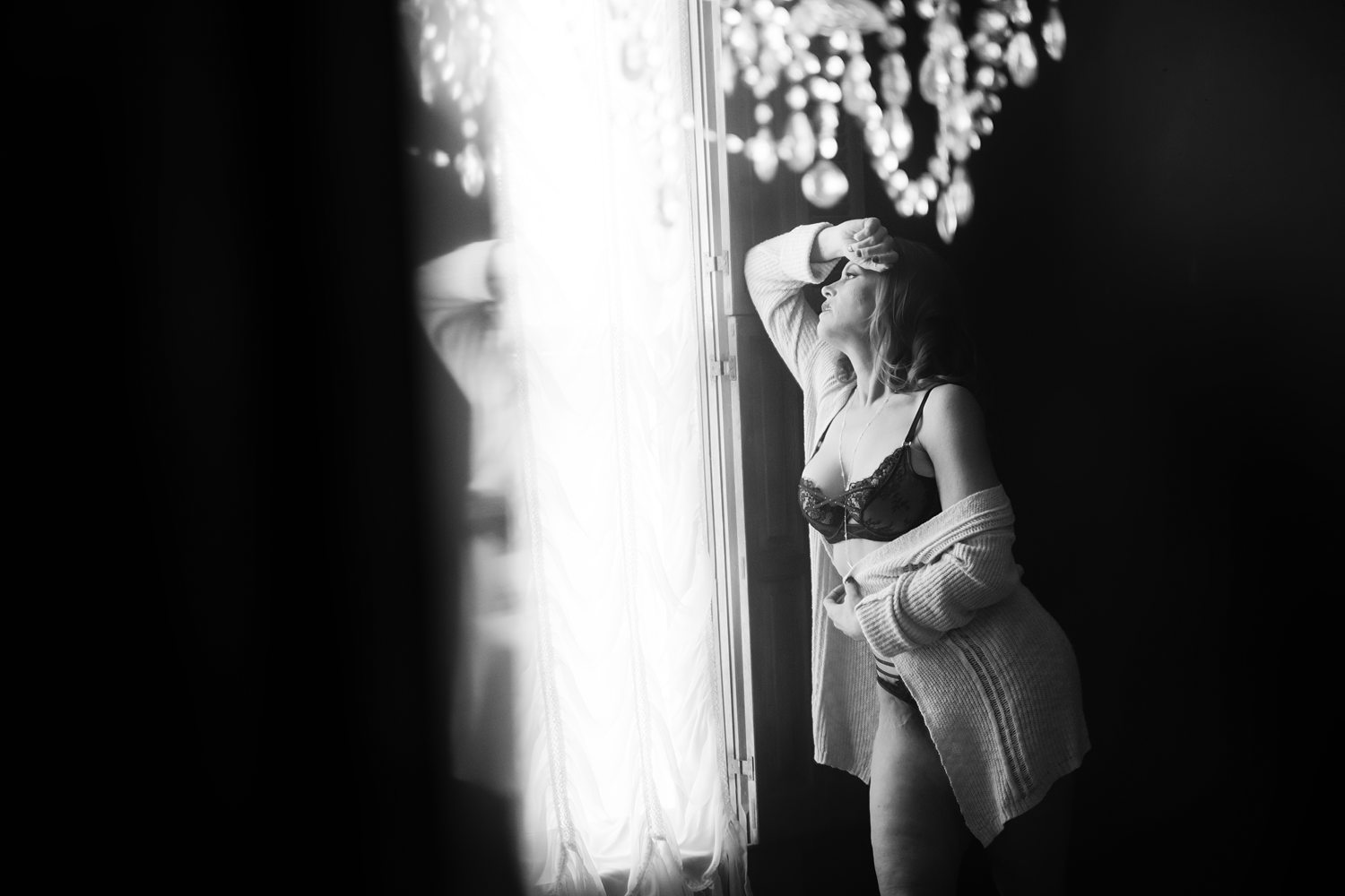 Classic boudoir portrait of woman in black lingerie looking longingly out of window during self-discovery boudoir session.