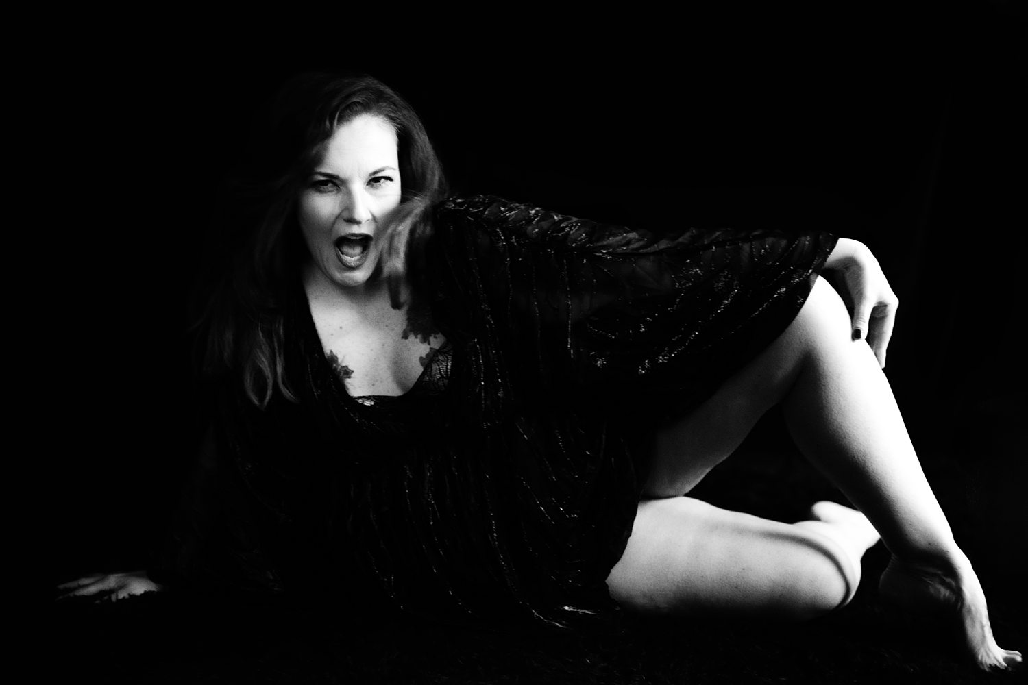 Editorial boudoir photo of woman sitting against a black background celebrating her confidence.