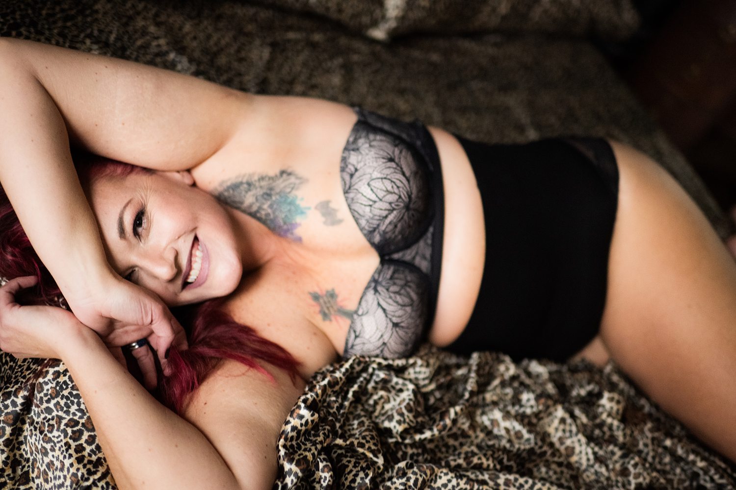 Playful boudoir photo of woman smiling joyfully at the camera wearing strapless bra and high-waisted underwear.