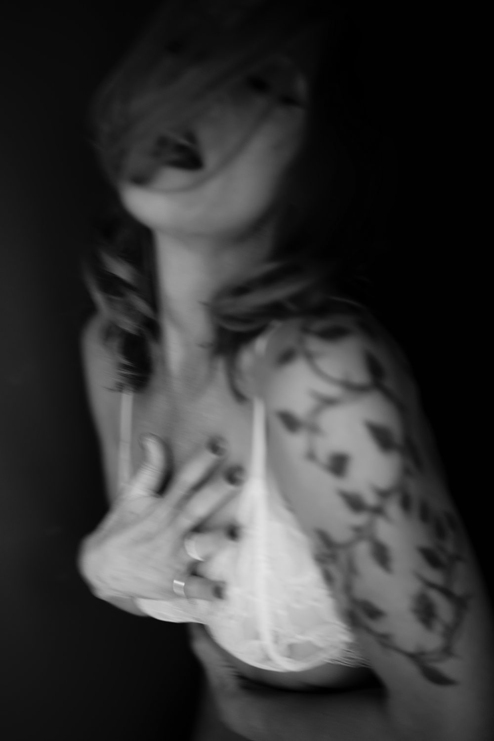 Sensual black-and-white boudoir photo of woman with tattoos with her hand placed on her chest during soulful boudoir session in Kalamazoo.