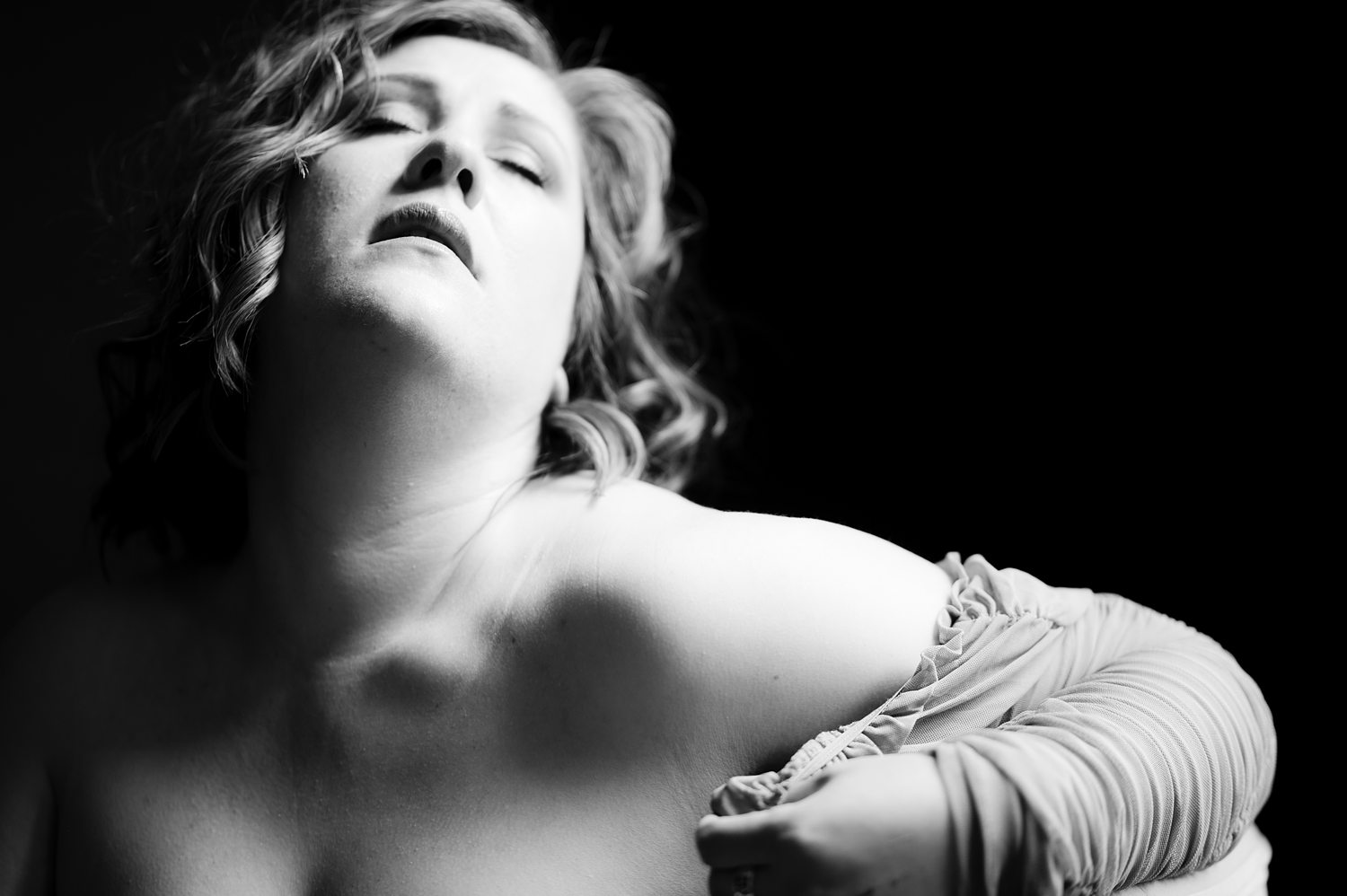 Soulful black-and-white close up of woman gently pulling on the sleeve of her dress during confidence building boudoir session.