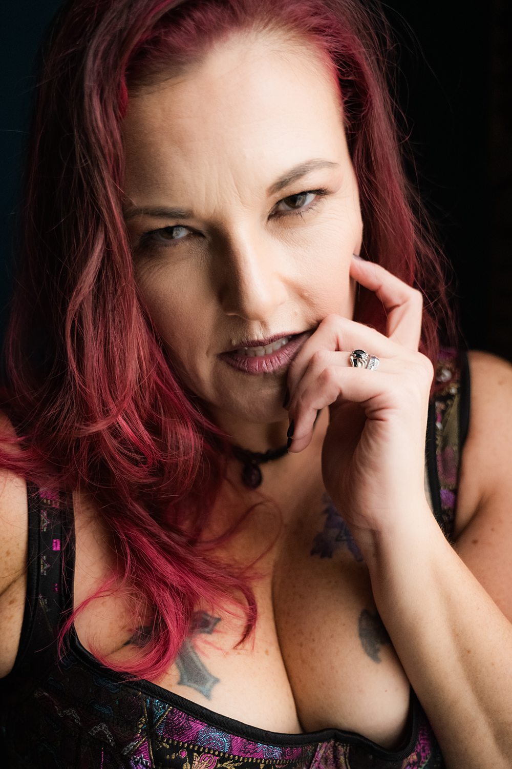 Sultry close up of woman with red hair and tattoos looking confidently at the camera during boudoir session for women in their 40s.