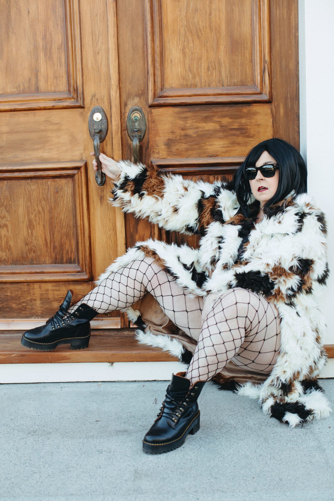 Betsy McCue Gibson, award-winning international boudoir photographer, wearing dramatic fur coat and fishnets sitting in front of wooden doors.
