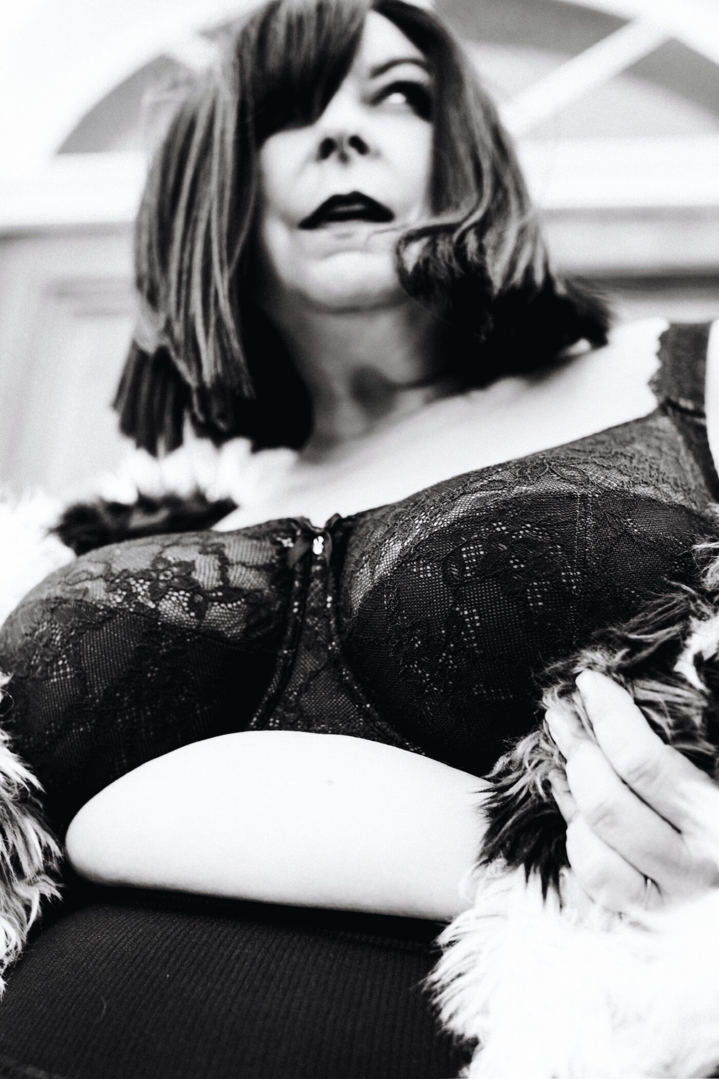 Dramatic black-and-white photo of Betsy McCue Gibson, award-winning international intimate boudoir editorial photographer in Kalamazoo Michigan, wearing black bra and fur coat.