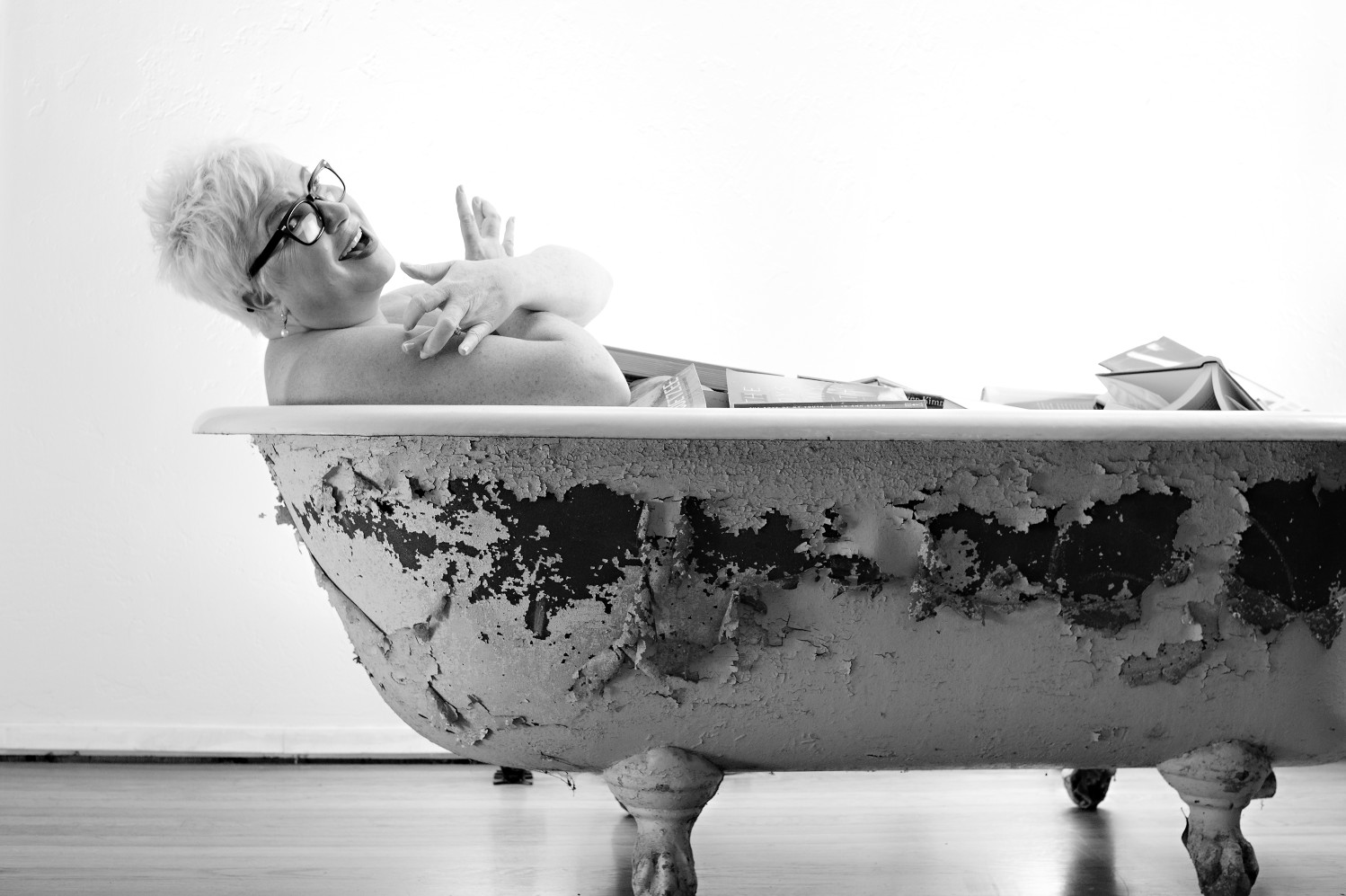 Black and white photo of woman wearing glasses smiling in an antique claw-foot tub.