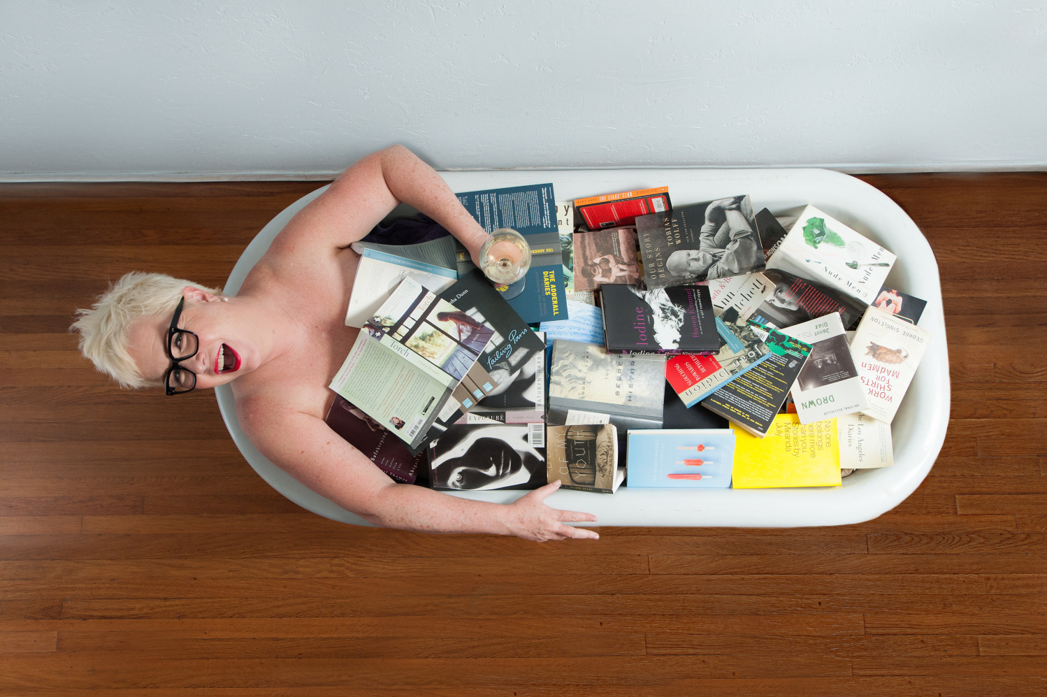 Overhead photo of woman laughing siting in a bathtub full of books.