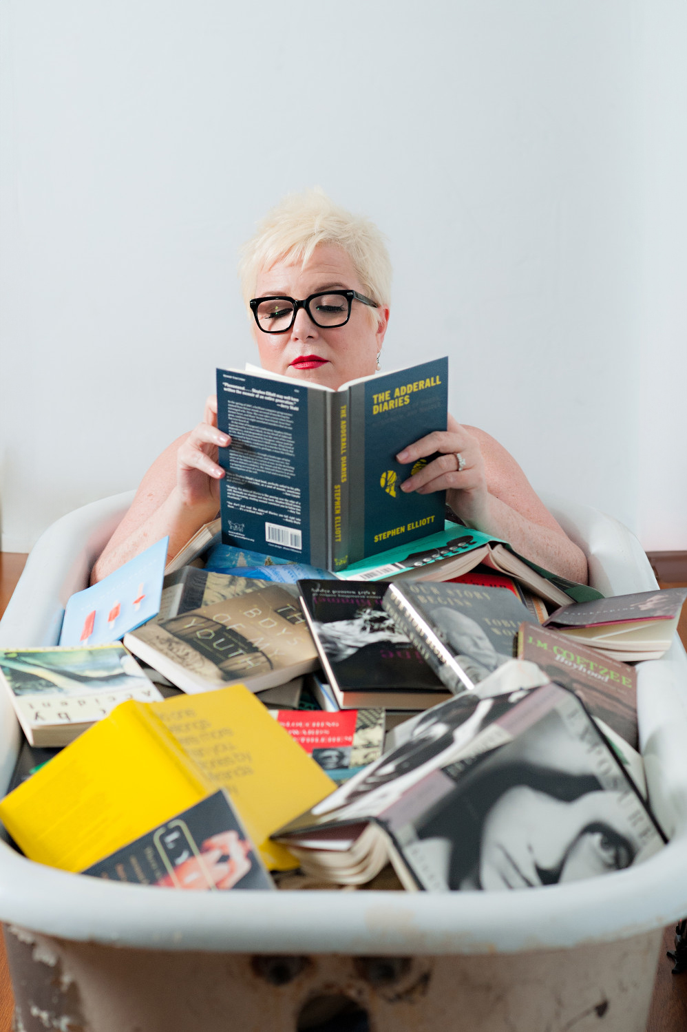 Unique boudoir photo of woman reading in a claw-foot tub filled with books photographed by Betsy McCue Pictures.