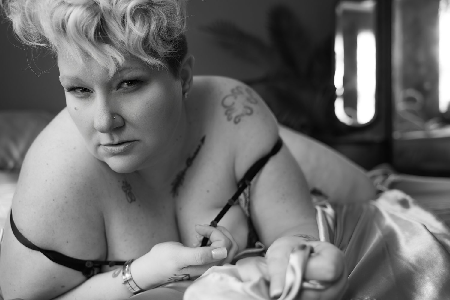 Black and white close up of woman looking confidently into the camera while in-the-sheets during soulful boudoir session in Kalamazoo.