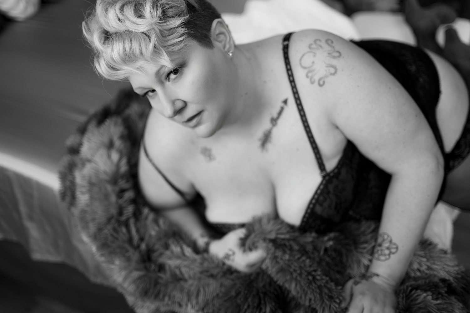 Woman soulfully looking at camera while gently holding a fur blanket, photographed in black and white.