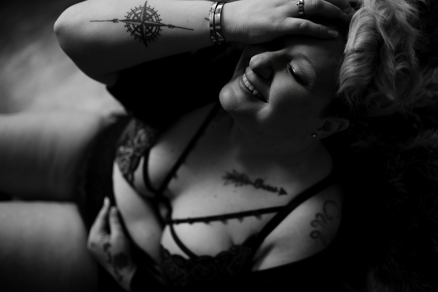 Woman with tattoos smiling sitting on floor during empowering boudoir session.