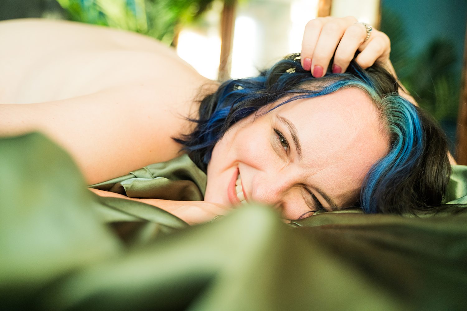 Smiling woman lying playfully in-the-sheets during an empowering boudoir session with Betsy McCue Pictures.